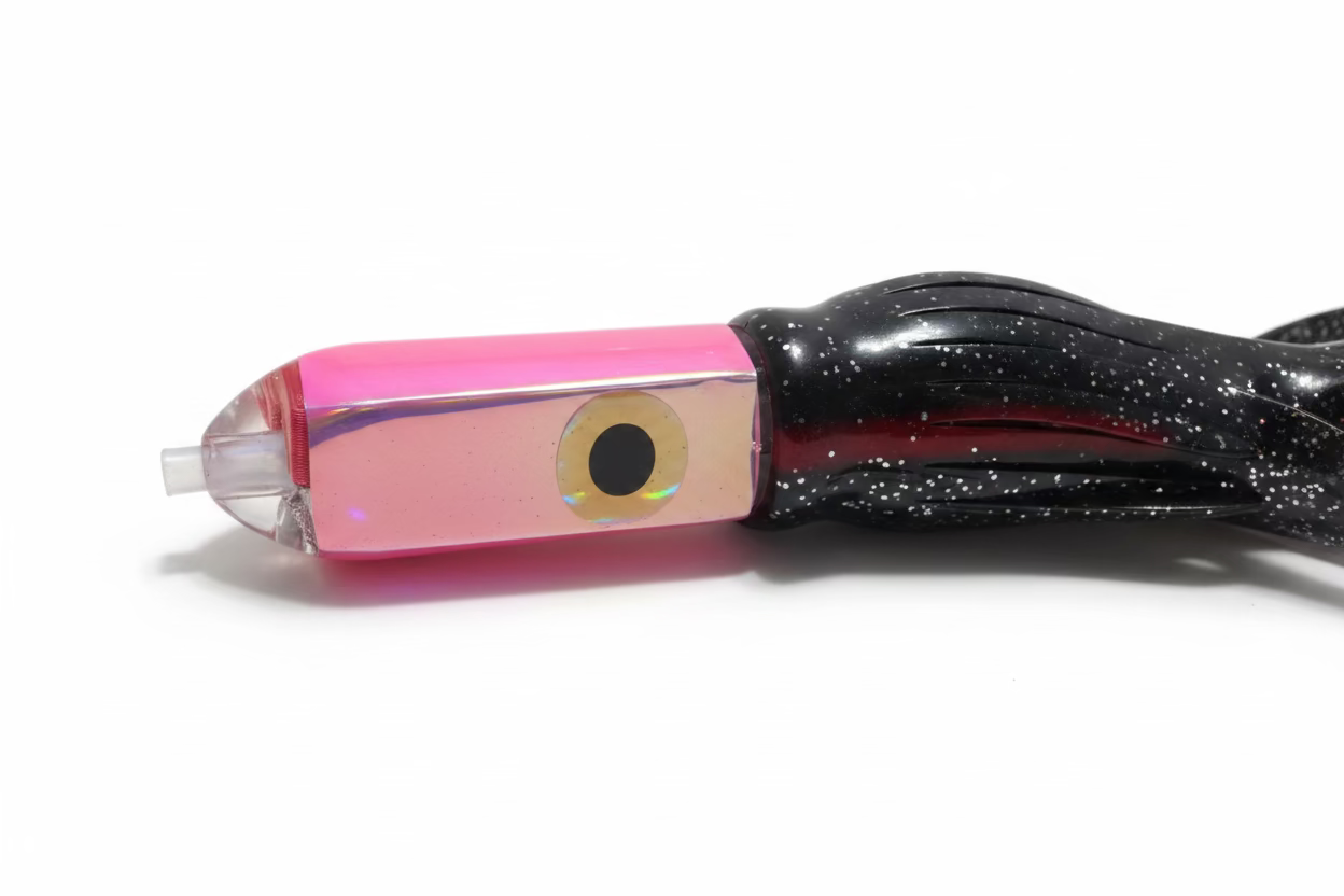 A close-up of a fishing lure with a glossy pink and iridescent body, a black skirt with white speckles, and a clear plastic nose on a beige fabric background.